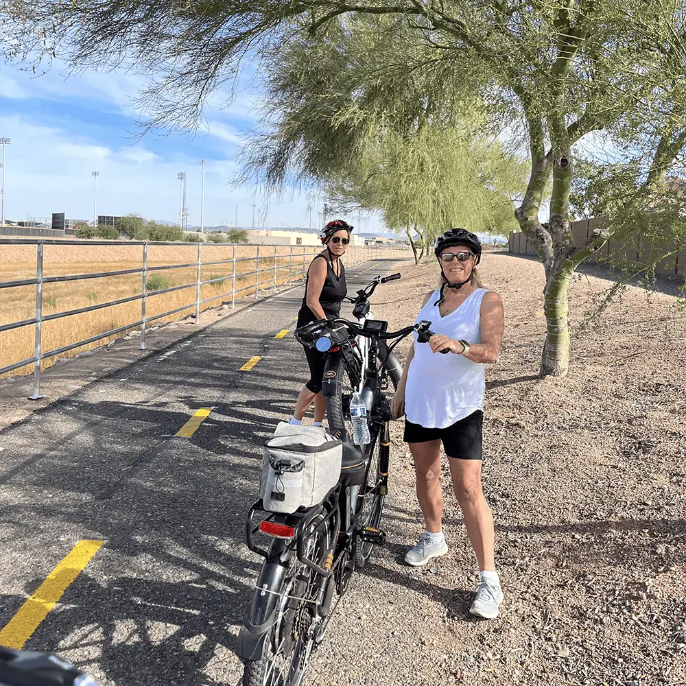 An elderly woman and a younger woman enjoy a ride on Smittys E-Bikes on a scenic bike trail outdoors.